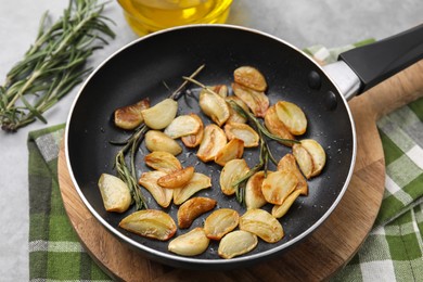 Photo of Frying pan with fried garlic cloves and rosemary on table