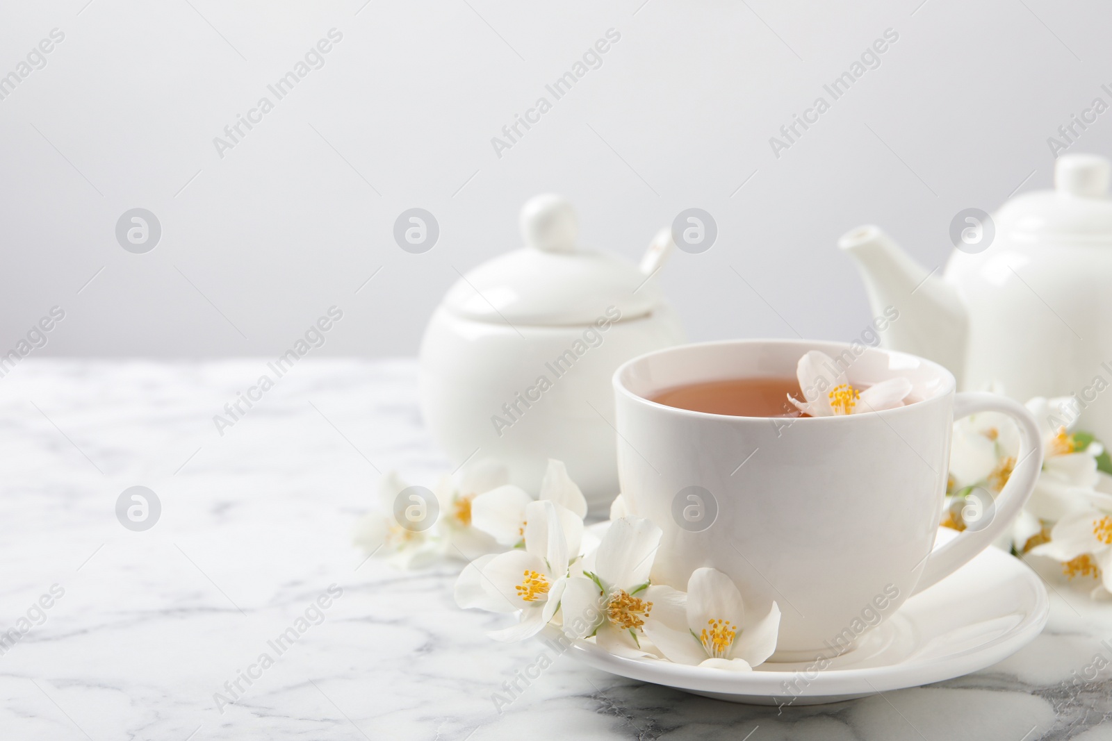 Photo of Aromatic jasmine tea and fresh flowers on white marble table, space for text