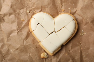 Photo of Broken heart shaped cookie on crumpled paper, top view. Relationship problems concept