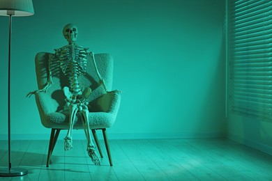 Waiting concept. Human skeleton sitting in armchair indoors, space for text