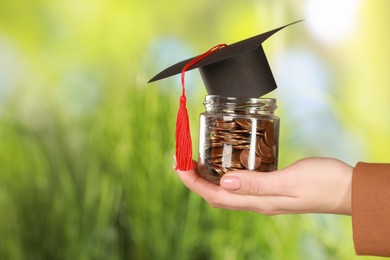 Woman holding glass jar of coins and graduation cap against blurred background, closeup with space for text. Scholarship concept