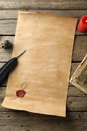 Sheet of old parchment paper with wax stamp, black feather, inkwell, vintage book and candle on wooden table, flat lay