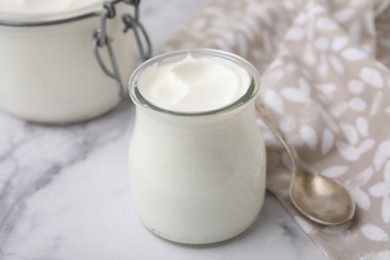 Delicious natural yogurt in glass jar and spoon on white marble table, closeup