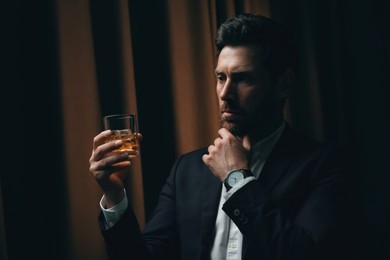Man in suit holding glass of whiskey with ice cubes on brown background