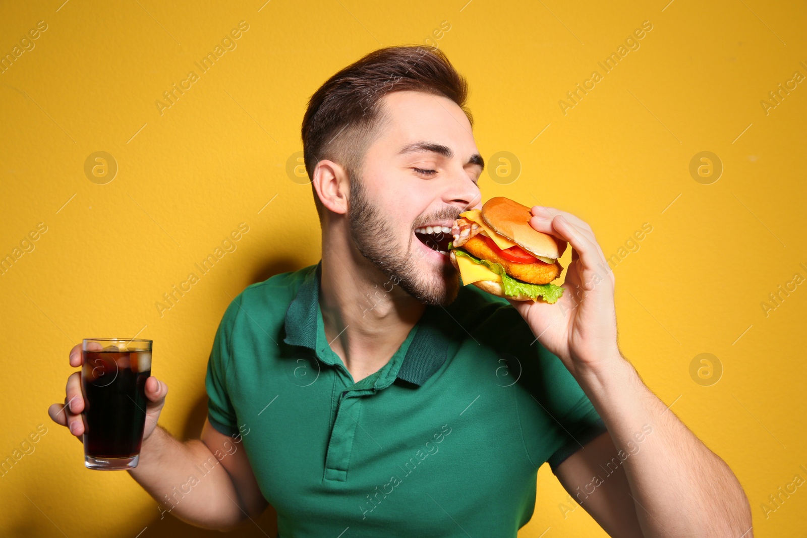 Photo of Handsome man with tasty burger and cola on color background