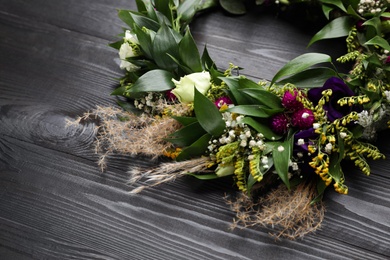 Photo of Beautiful wreath made of flowers and leaves on wooden table, closeup