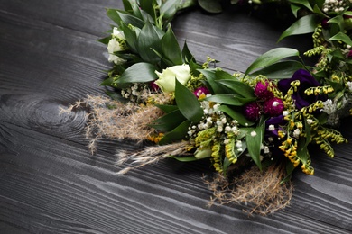 Beautiful wreath made of flowers and leaves on wooden table, closeup