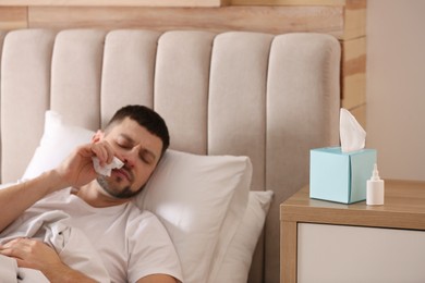 Photo of Ill man at home, focus on nasal spray and box of tissues