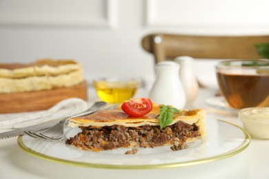 Piece of delicious pie with minced meat, tomato and basil served on white table, closeup