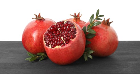 Fresh pomegranates and green leaves on black wooden table against white background