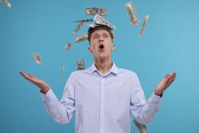 Handsome man under money shower on light blue background