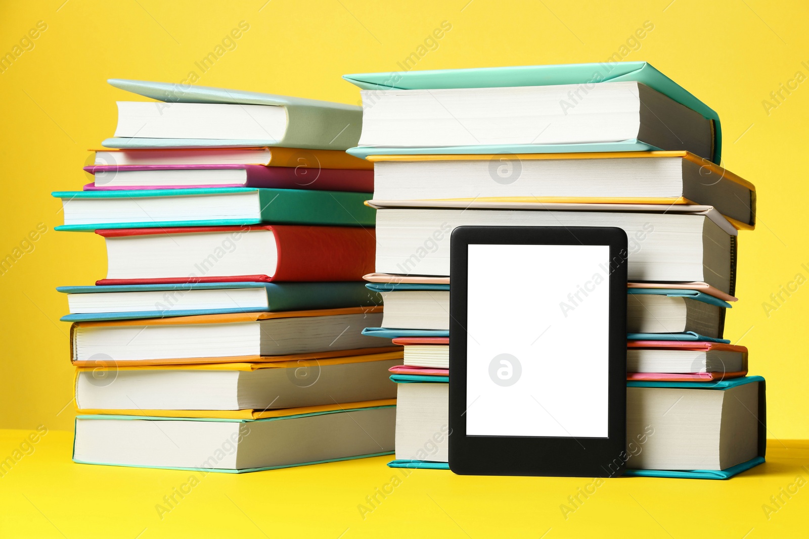 Photo of Modern e-book reader and stacks of hard cover books on yellow background