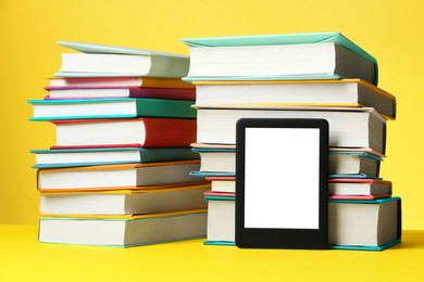 Modern e-book reader and stacks of hard cover books on yellow background