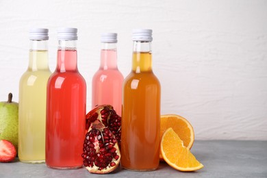 Delicious kombucha in glass bottles and fresh fruits on grey table against white background