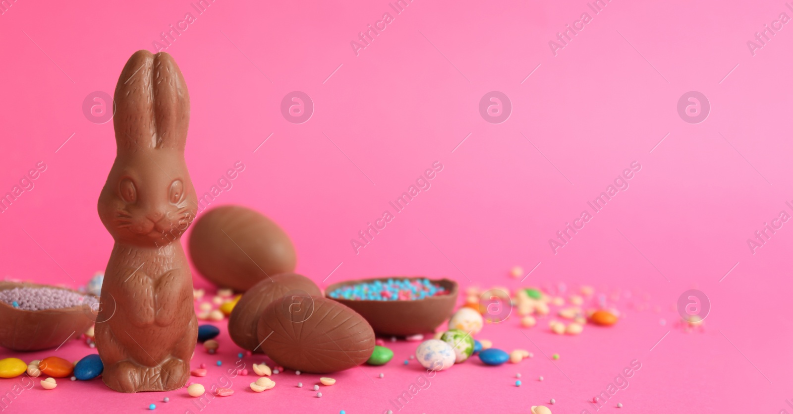 Photo of Chocolate Easter bunny, eggs and candies on pink background. Space for text