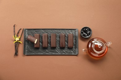 Glazed curd cheese bars, vanilla pods and tea on light brown background, flat lay