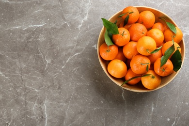 Fresh tangerines with green leaves on grey table, top view. Space for text