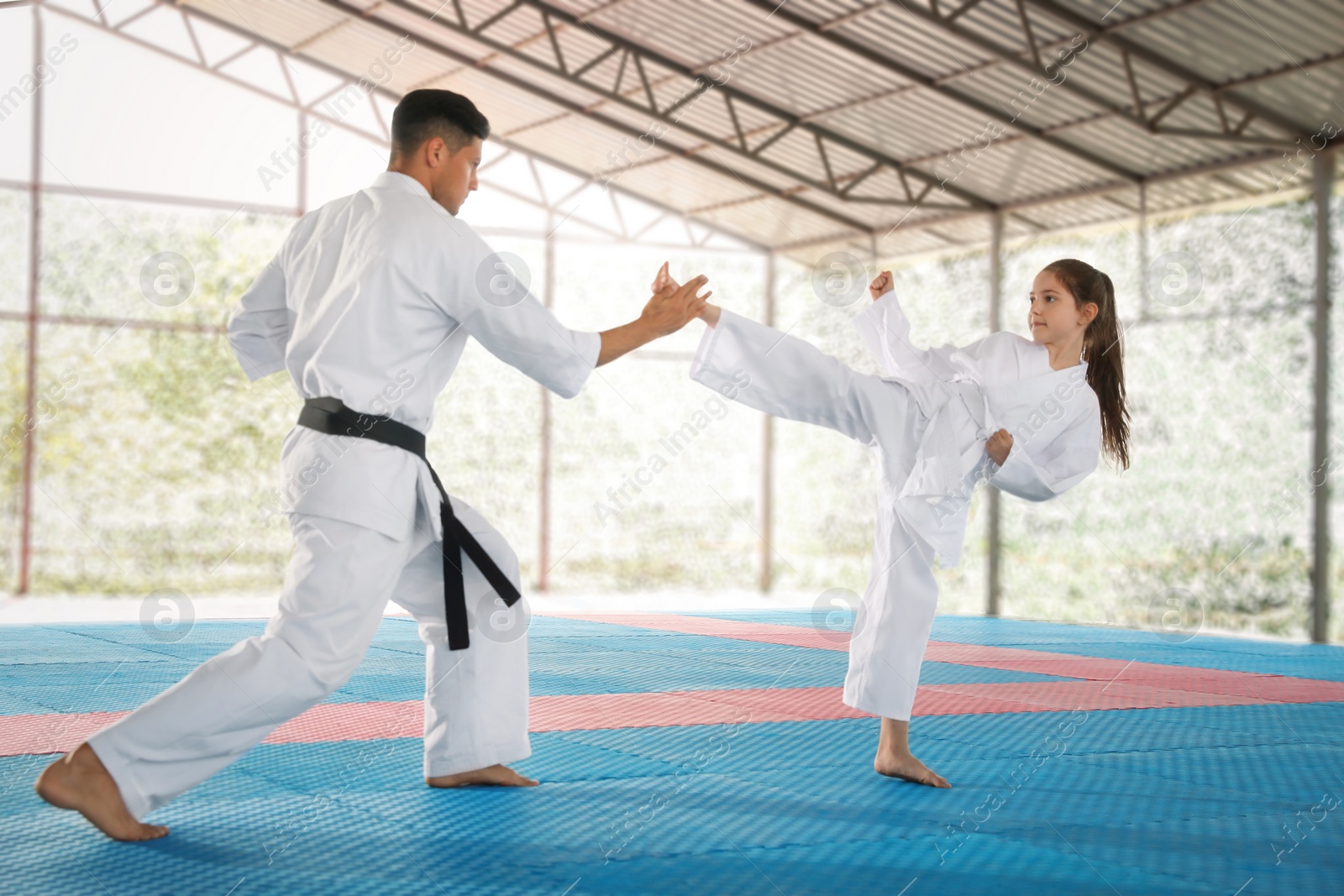 Photo of Girl practicing karate with coach on tatami outdoors