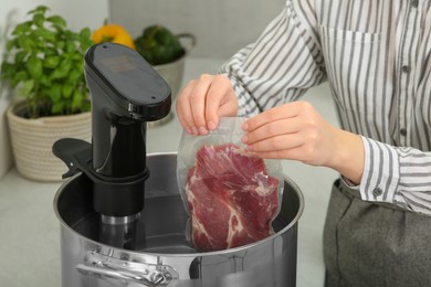 Photo of Woman putting vacuum packed meat into pot in kitchen, closeup. Thermal immersion circulator for sous vide cooking