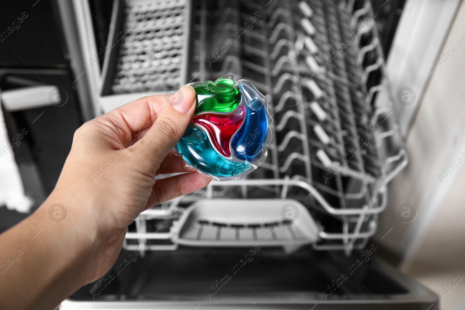 Photo of Woman putting detergent pod into open clean modern empty automatic dishwasher machine in kitchen, closeup