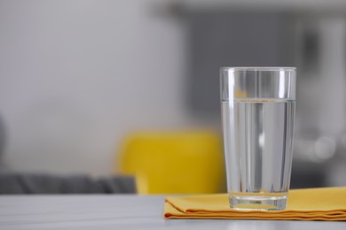 Photo of Glass of water and napkin on white table against blurred background. Space for text