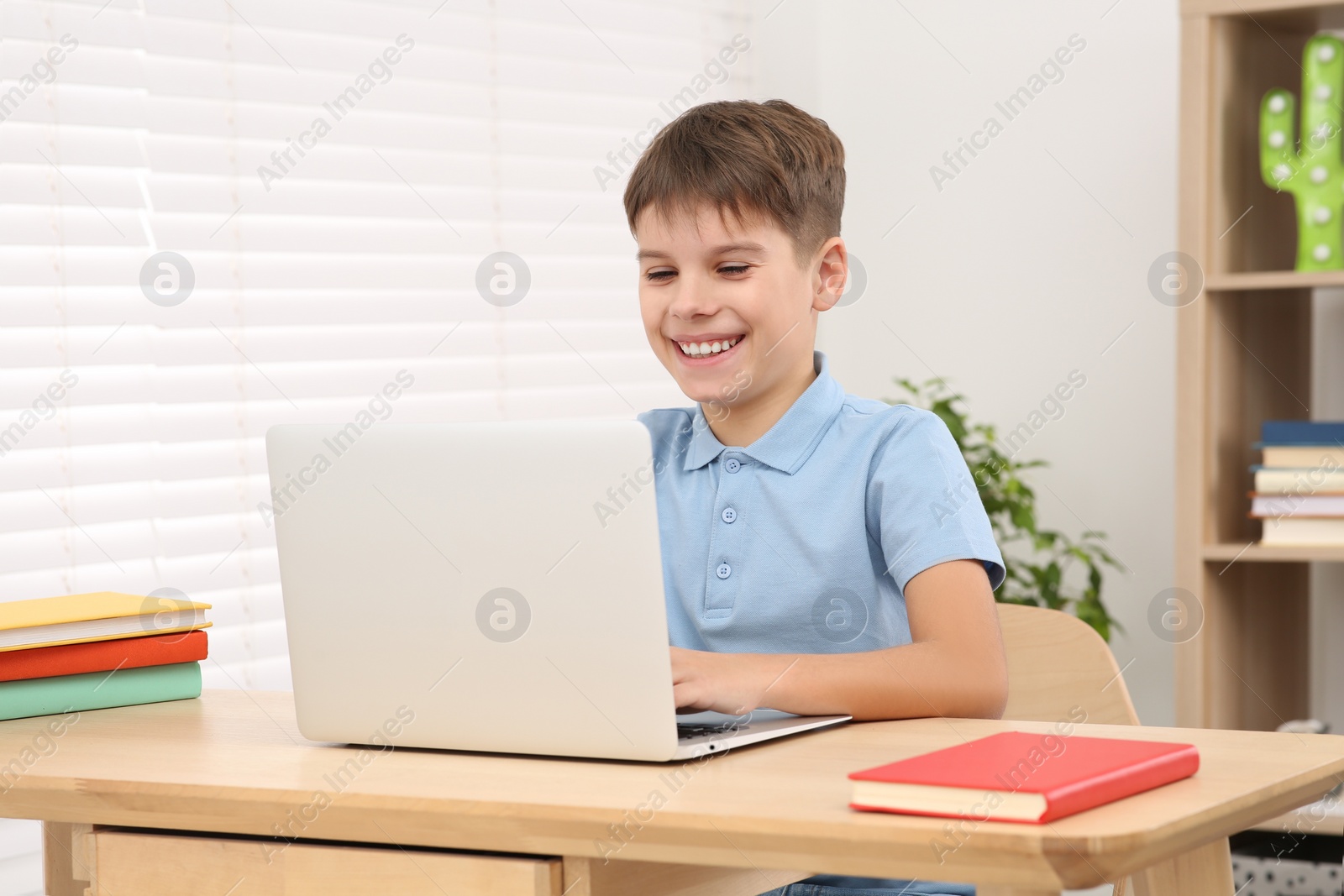 Photo of Smiling boy using laptop at desk in room. Home workplace