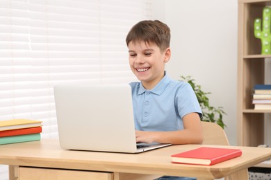 Smiling boy using laptop at desk in room. Home workplace