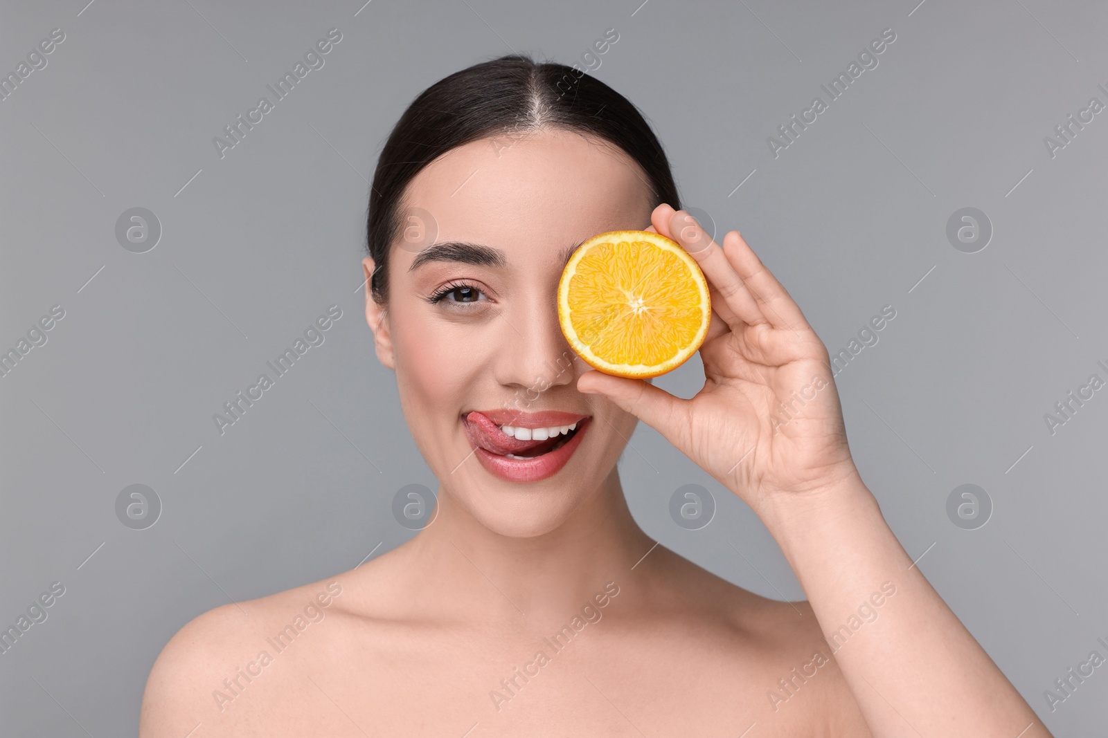 Photo of Beautiful young woman with piece of orange on grey background