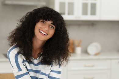 Photo of Portrait of beautiful woman with curly hair in kitchen. Attractive lady smiling and looking into camera. Space for text