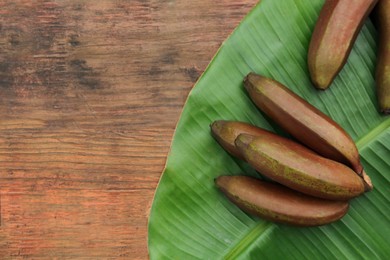 Delicious purple bananas and fresh leaf on wooden table, flat lay. Space for text