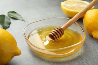 Photo of Sweet honey and fresh lemons on grey table, closeup