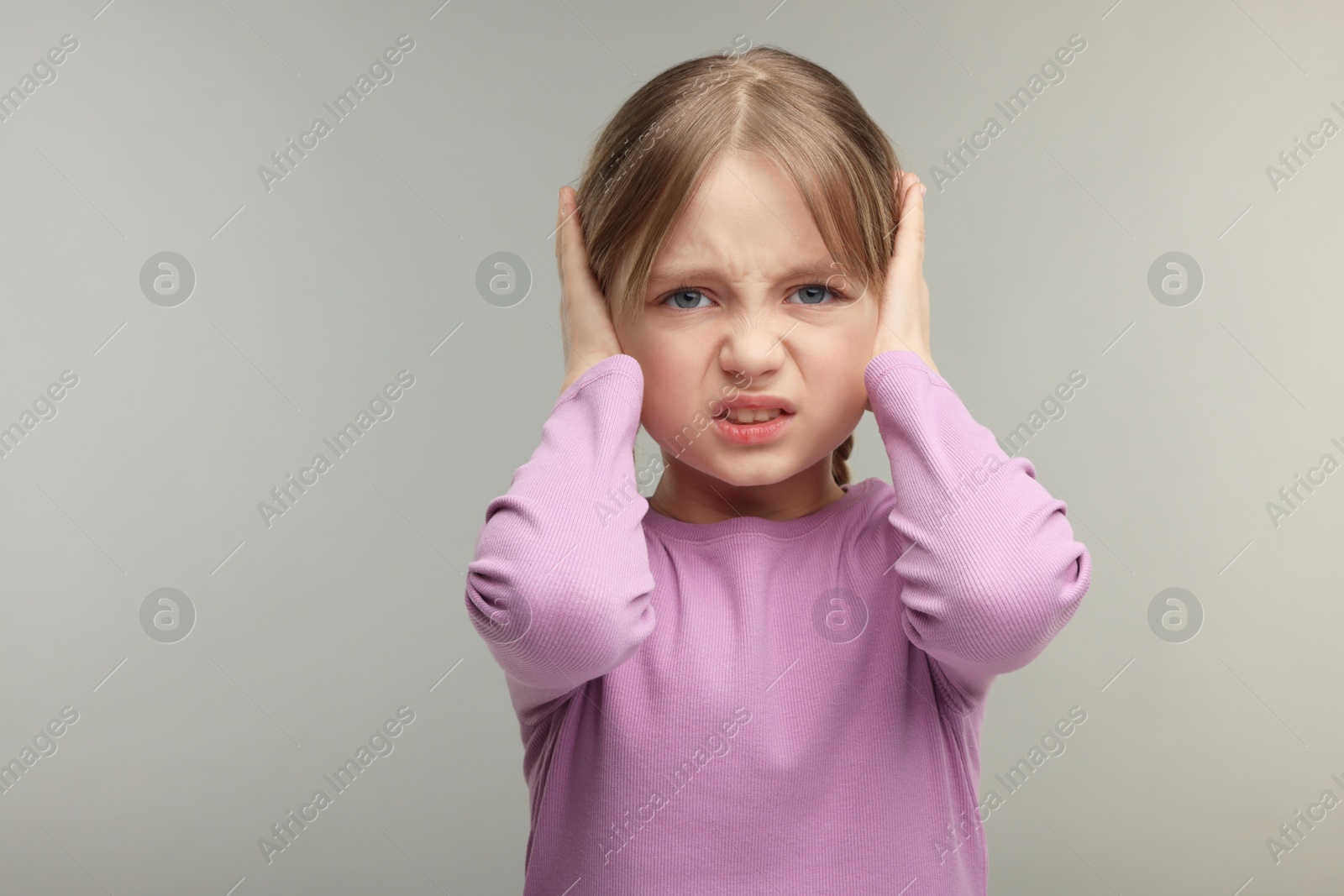 Photo of Hearing problem. Little girl suffering from ear pain on grey background