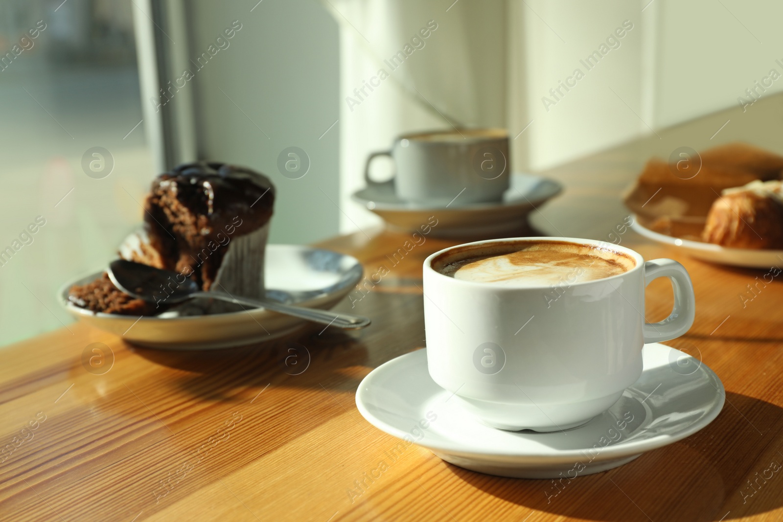 Photo of Cup of fresh aromatic coffee and cupcake at table in cafe