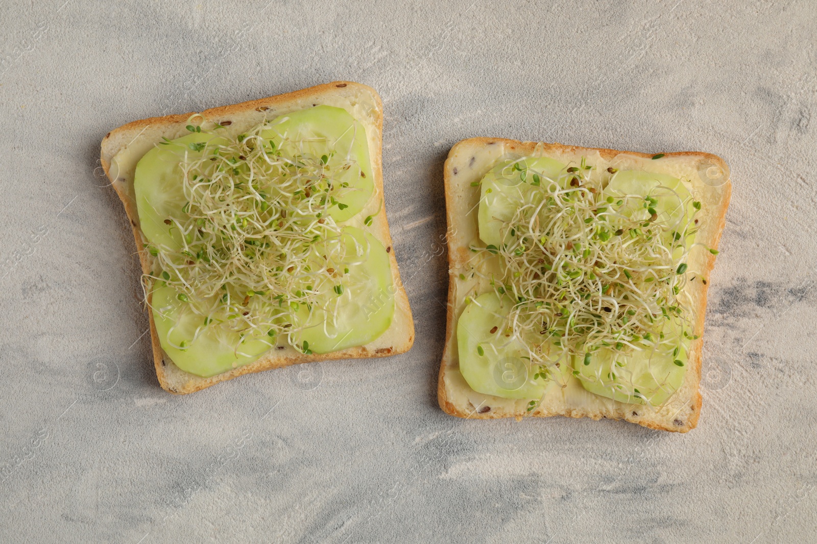 Photo of Tasty sandwiches with cucumber and microgreens on textured table, top view