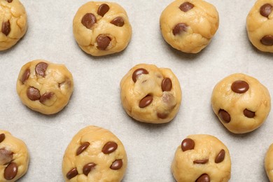 Photo of Unbaked chocolate chip cookies on parchment paper, flat lay