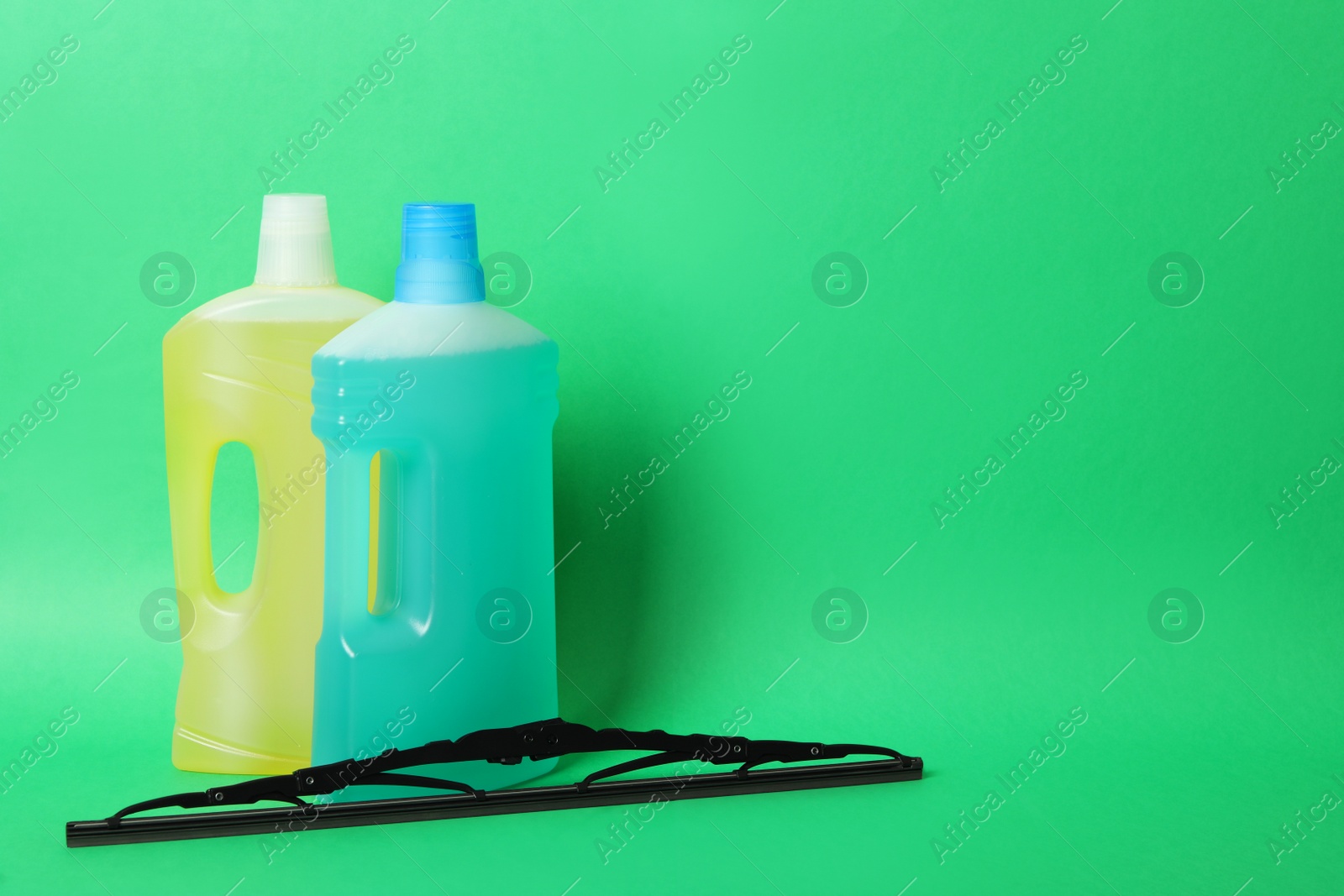 Photo of Bottles of windshield washer fluids and wiper on green background. Space for text