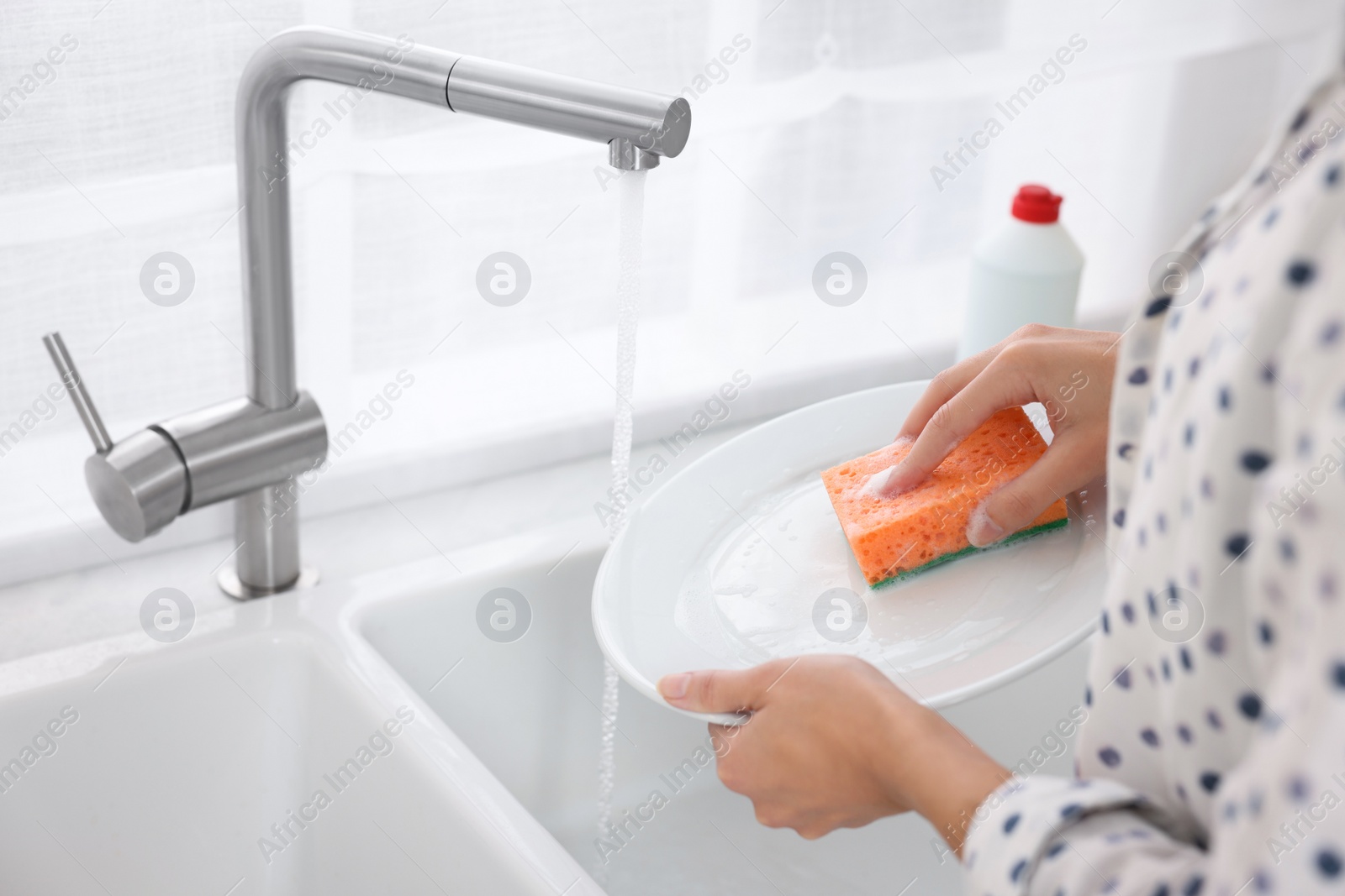 Photo of Woman washing plate above sink in modern kitchen, closeup