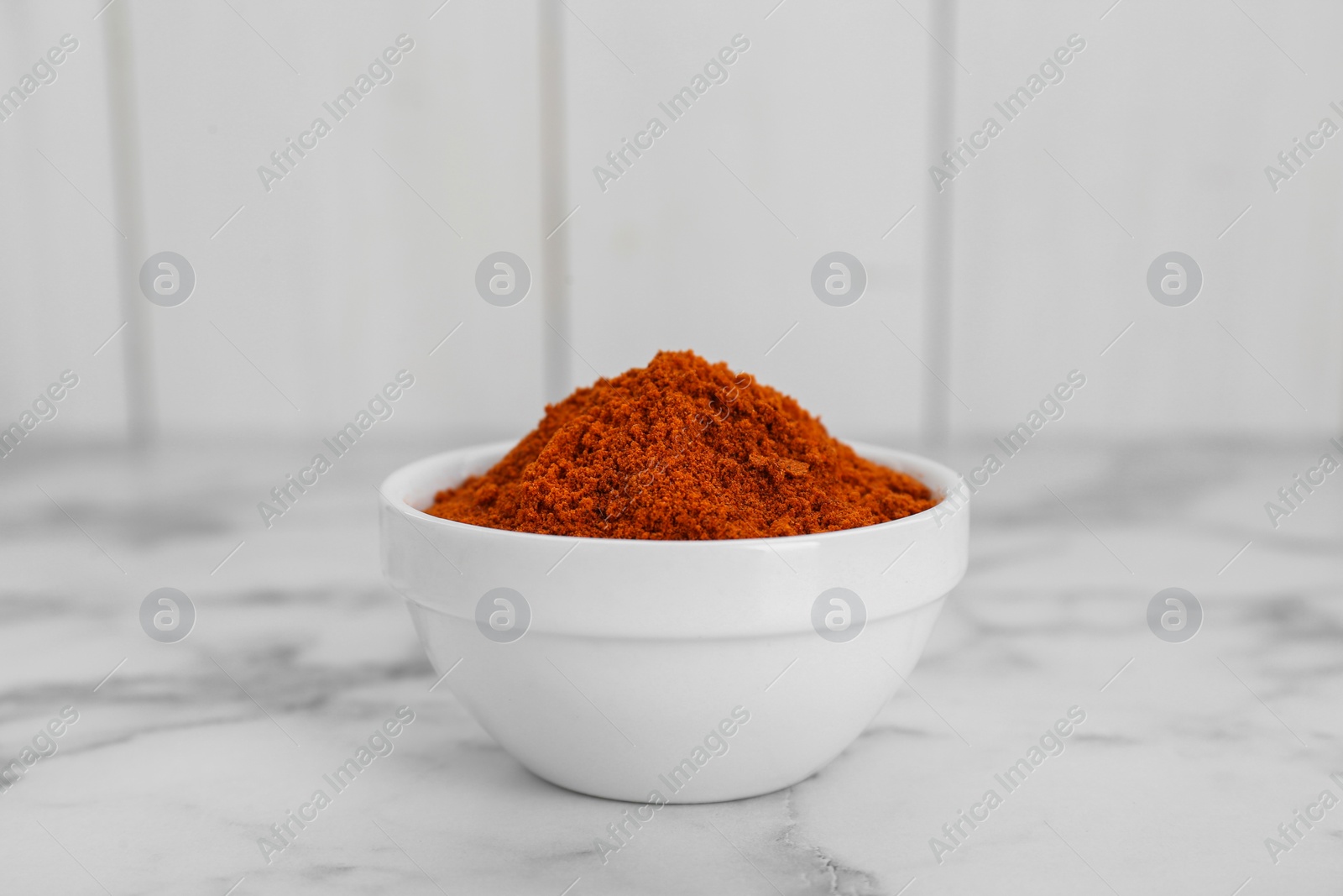 Photo of Bowl with aromatic paprika powder on white marble table