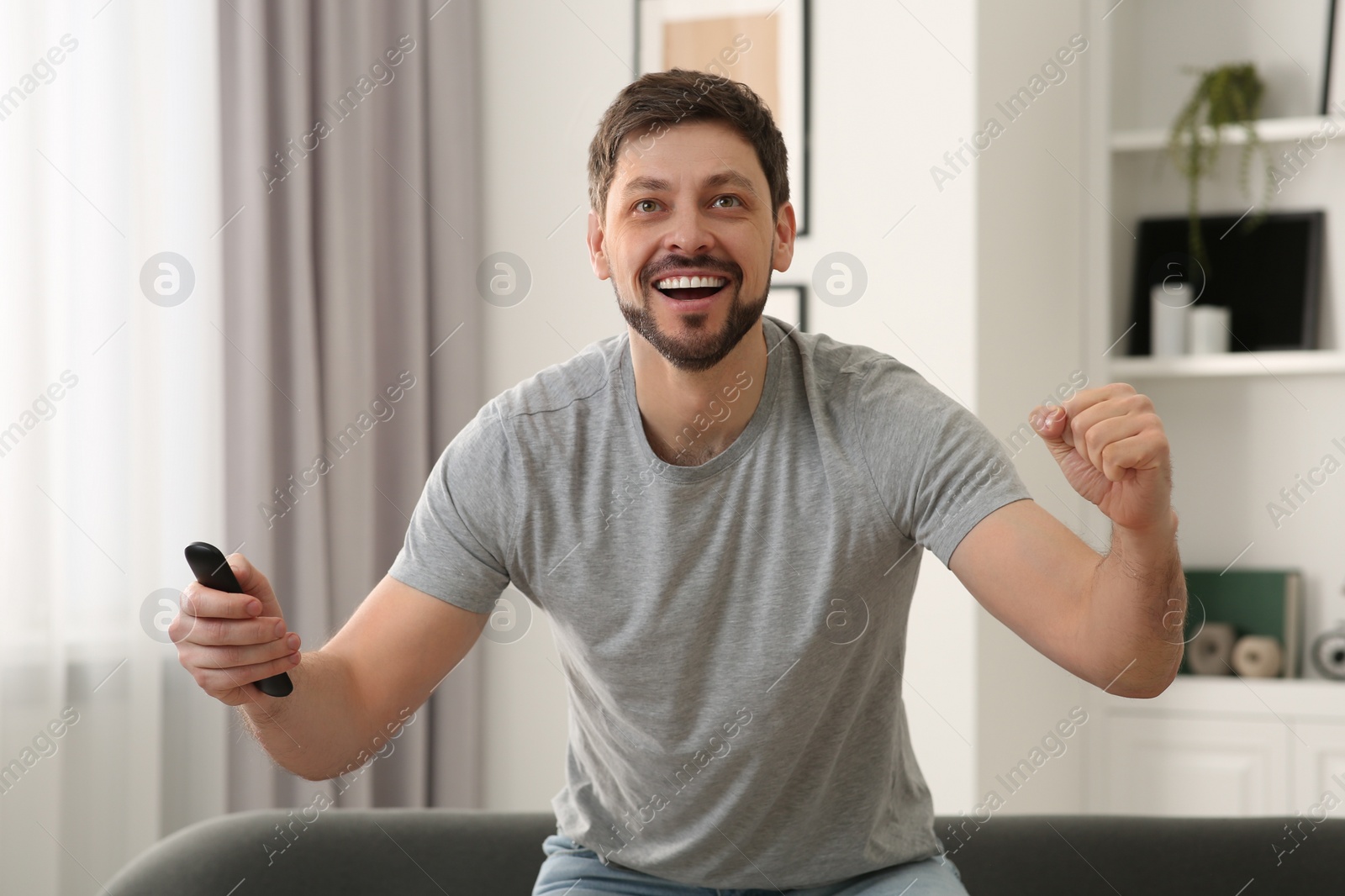 Photo of Emotional man holding remote controller and watching TV at home