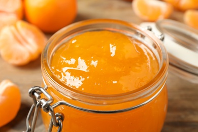 Tasty tangerine jam in glass jar on table, closeup