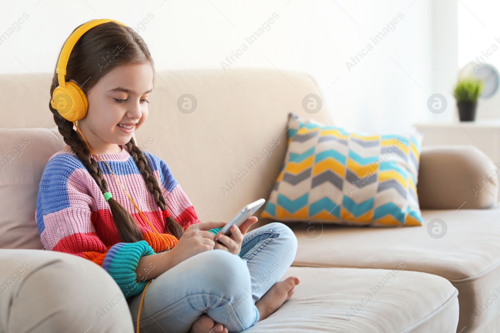 Photo of Cute child with headphones and mobile phone on sofa indoors. Space for text