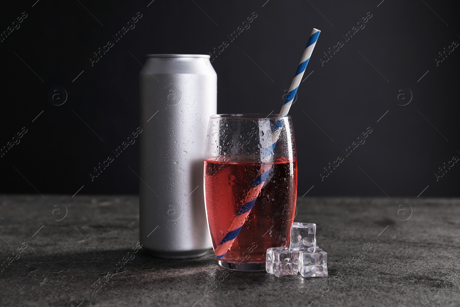 Photo of Energy drink in glass, aluminium can and ice cubes on grey table