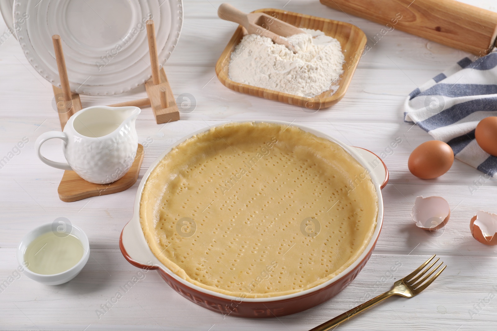 Photo of Pie tin with fresh dough and ingredients on white wooden table. Making quiche