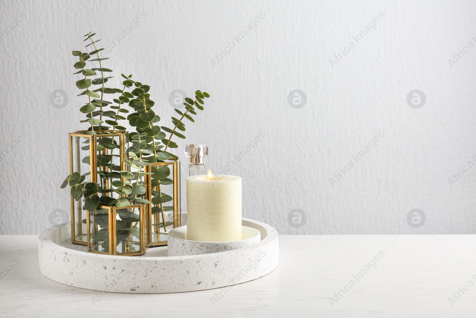Photo of Stylish tender composition with burning candle and plants on white wooden table against light background, space for text. Cozy interior element