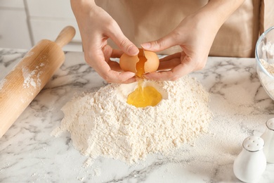 Photo of Woman breaking egg over pile of flour on table in kitchen