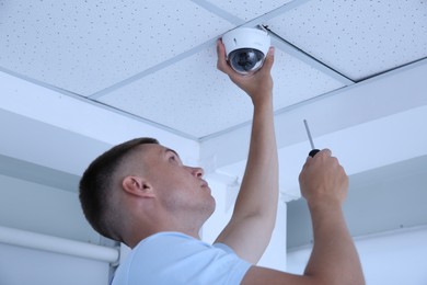 Photo of Technician with screwdriver installing CCTV camera on ceiling indoors