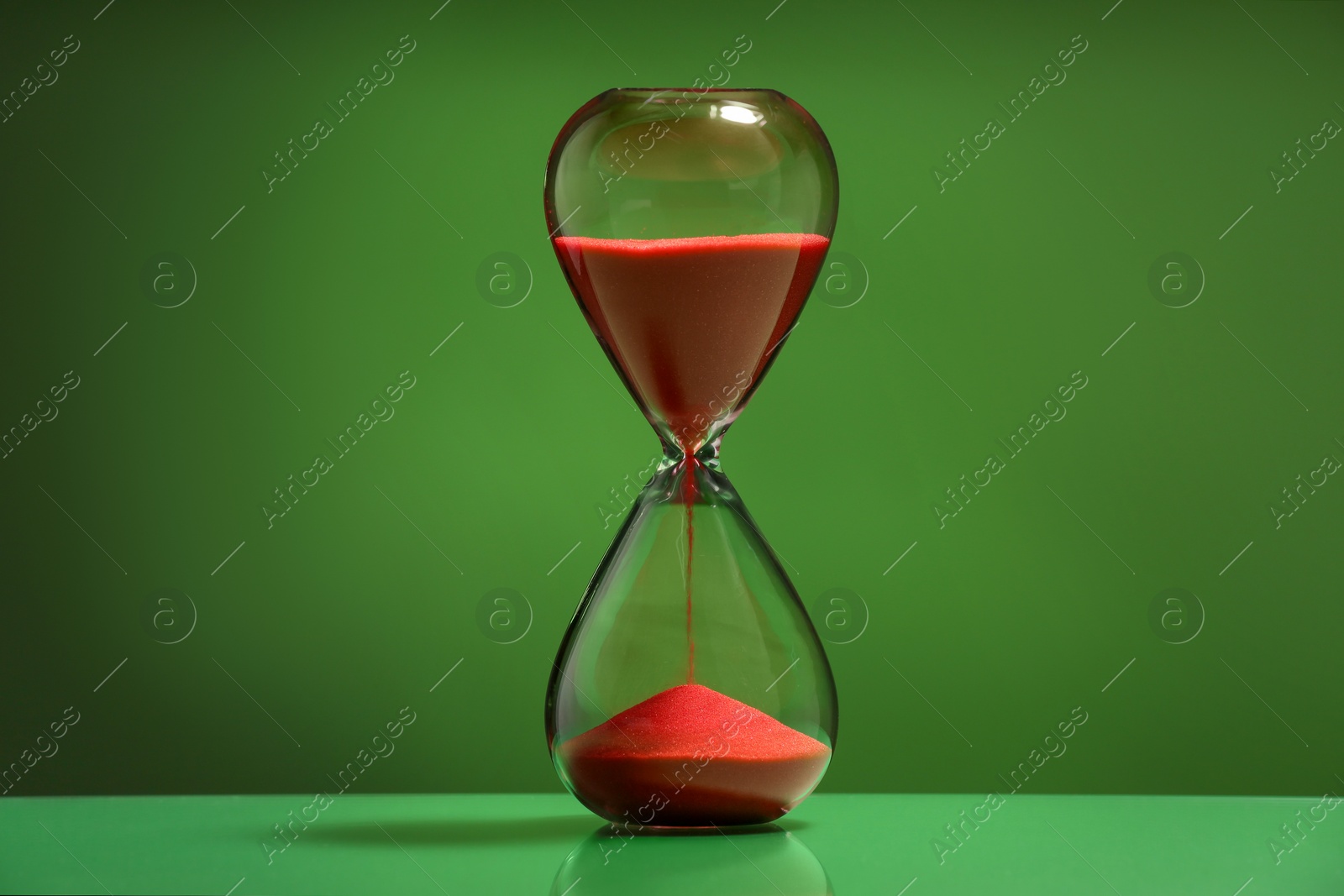 Photo of Hourglass with red flowing sand on green background