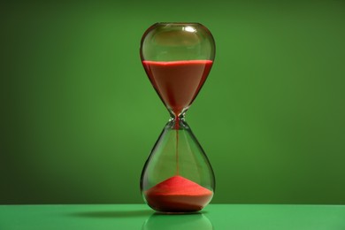 Hourglass with red flowing sand on green background