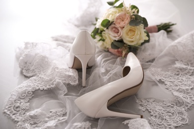 Photo of Pair of white high heel shoes, veil and wedding bouquet on grey background