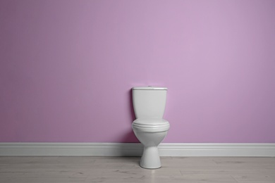 Photo of New ceramic toilet bowl near color wall with space for text